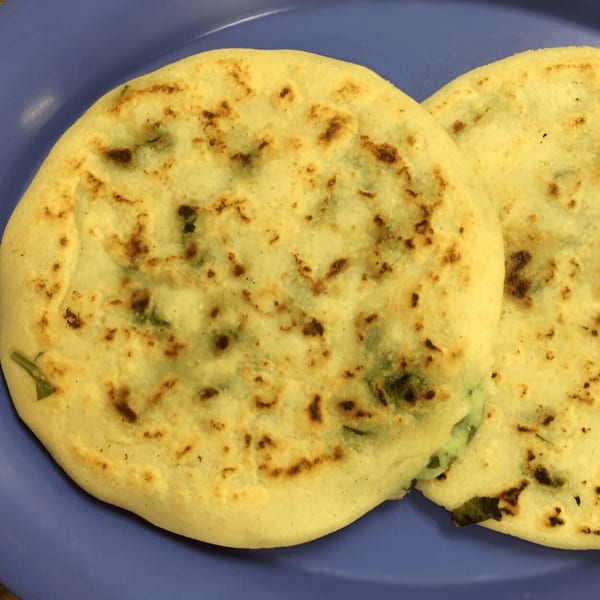 Two golden-brown pupusas with green specks, likely cheese and herbs, on a purple plate.