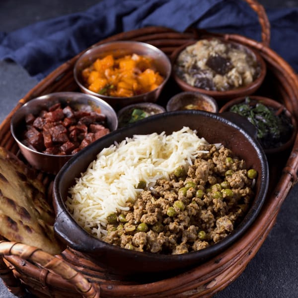 A woven tray holds various Salvadoran dishes, including rice, ground meat with peas, and other sides.