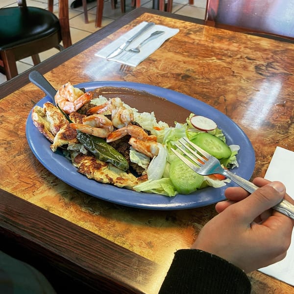 A blue plate of Salsabor's Salvadoran shrimp, steak, and pupusas with salad, held by a person.